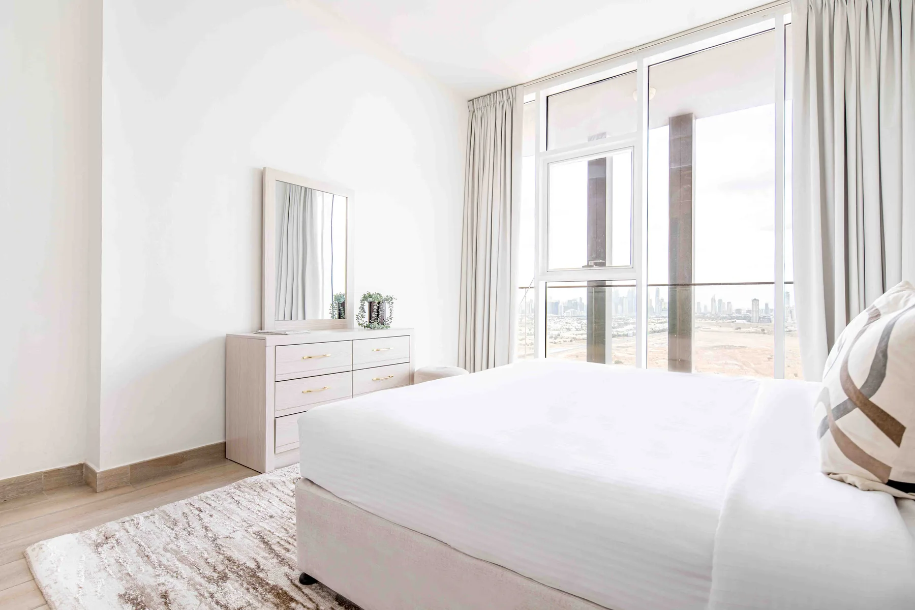 A bright bedroom with a bed beside large windows and a dresser.