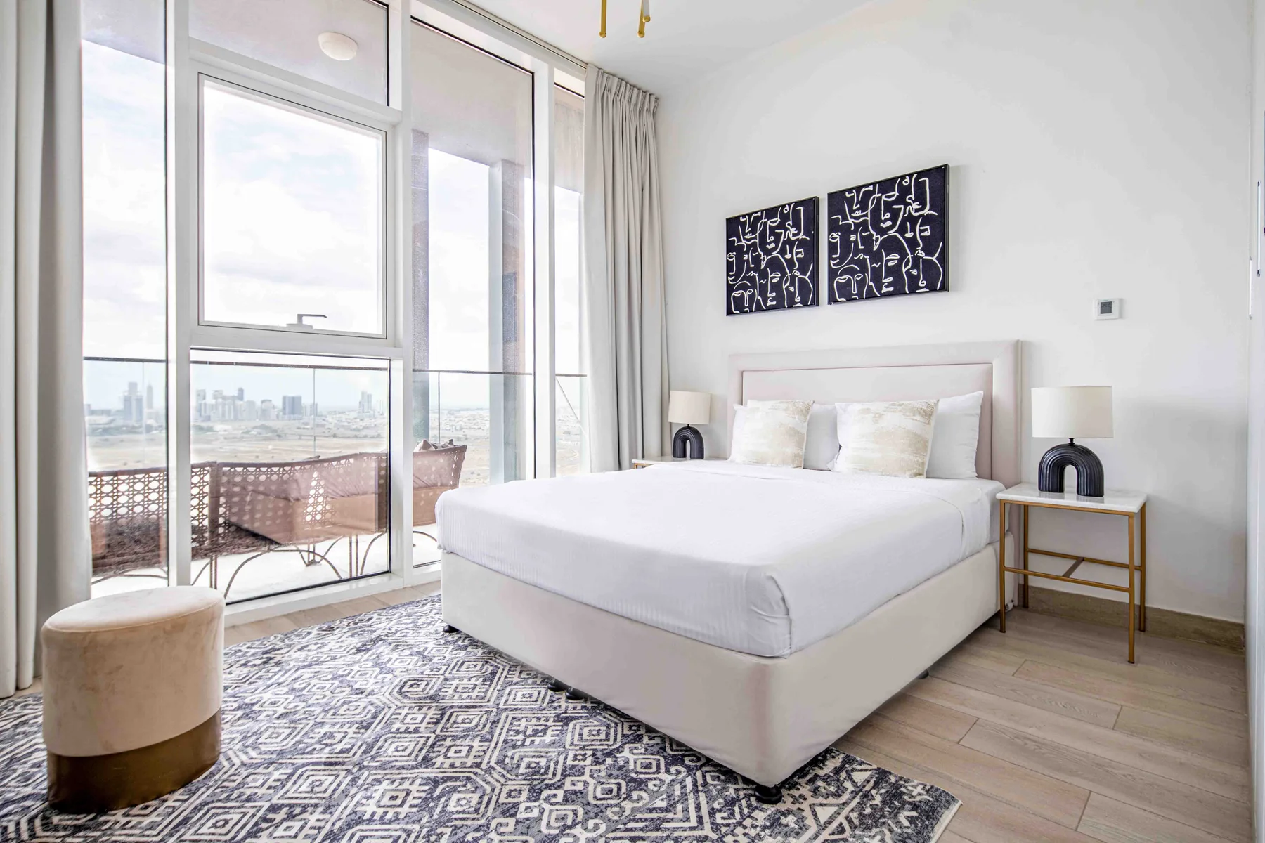 A bright bedroom with a bed beside large windows overlooking a balcony.