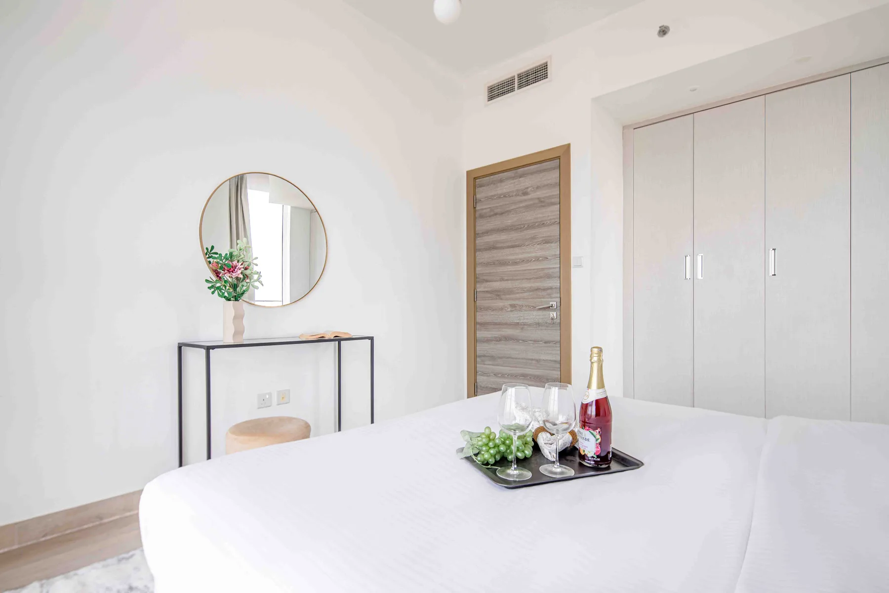 A bright bedroom with a bed, mirrored wall, and built-in storage.
