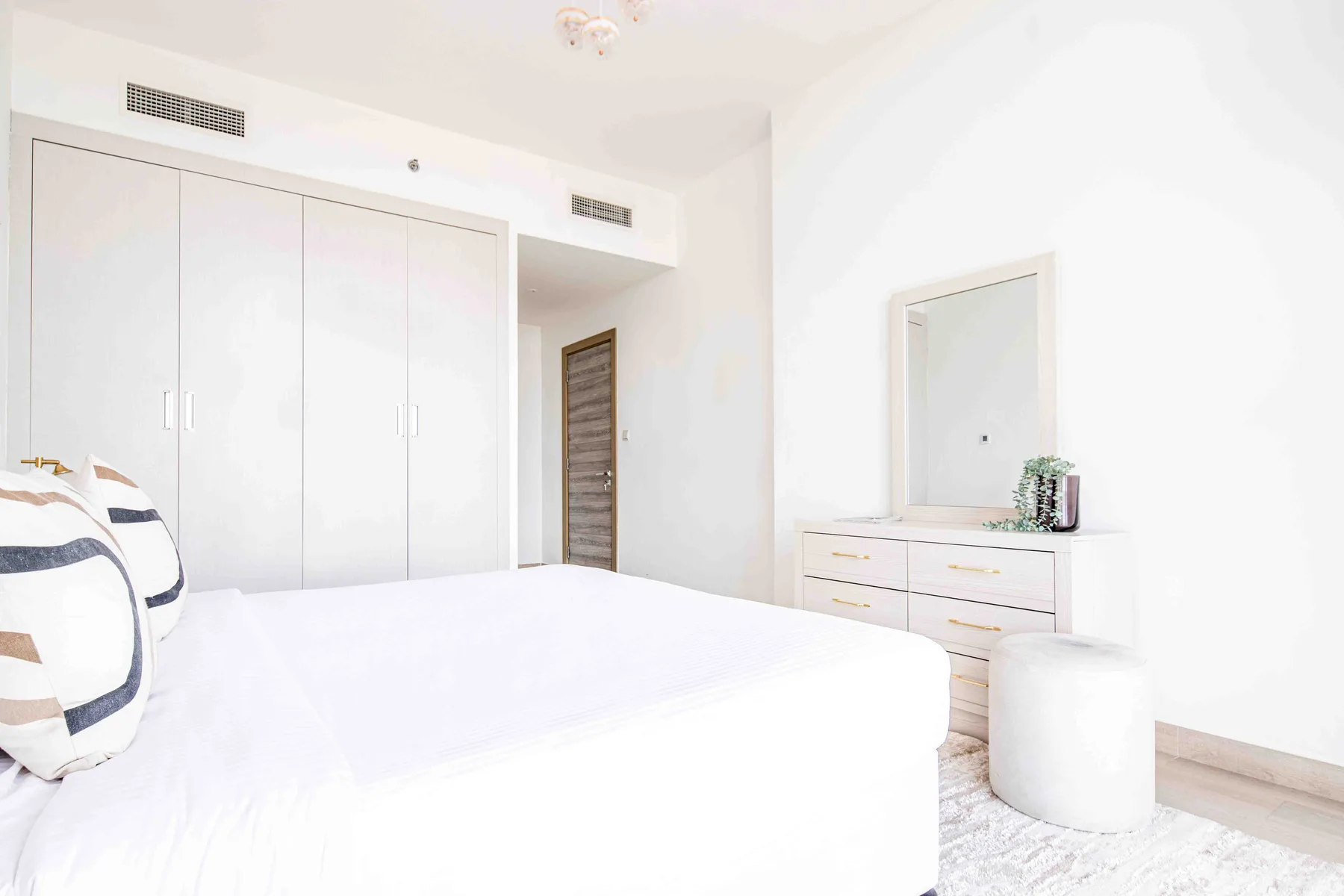 A bright bedroom with a bed, built-in wardrobes, and a dresser with a mirror.
