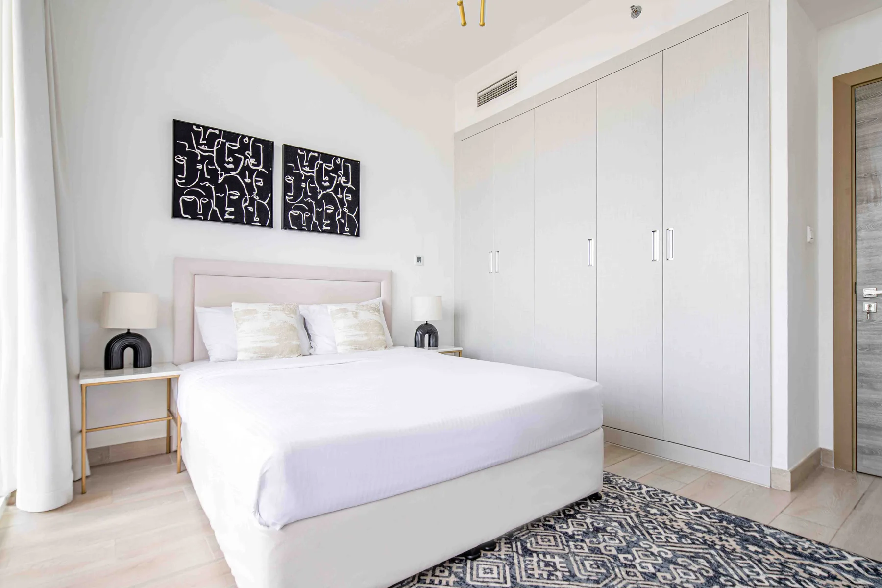 A bright bedroom with a bed, bedside tables, and a large built-in wardrobe.