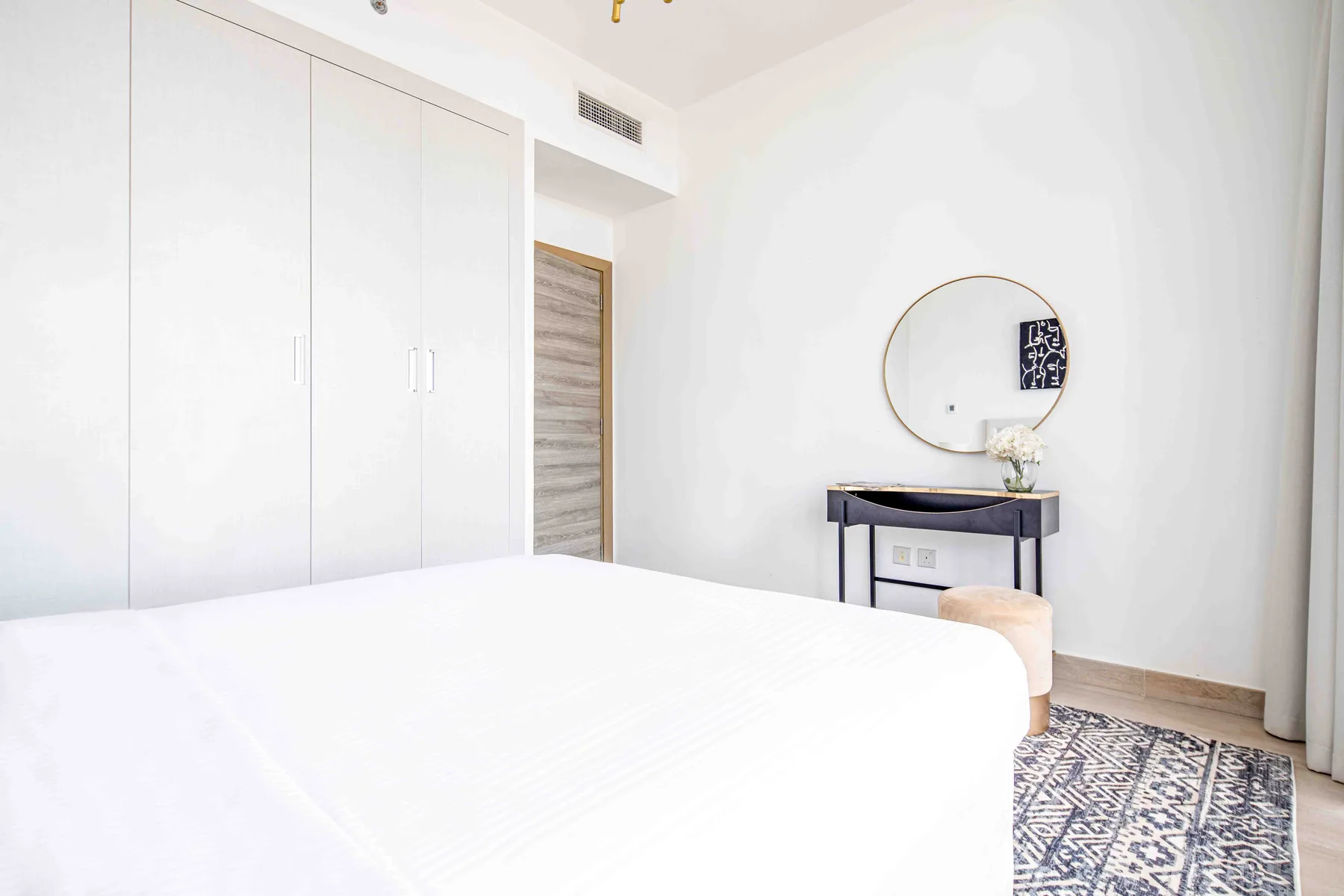 A bright bedroom with a bed, wardrobe, and console table.