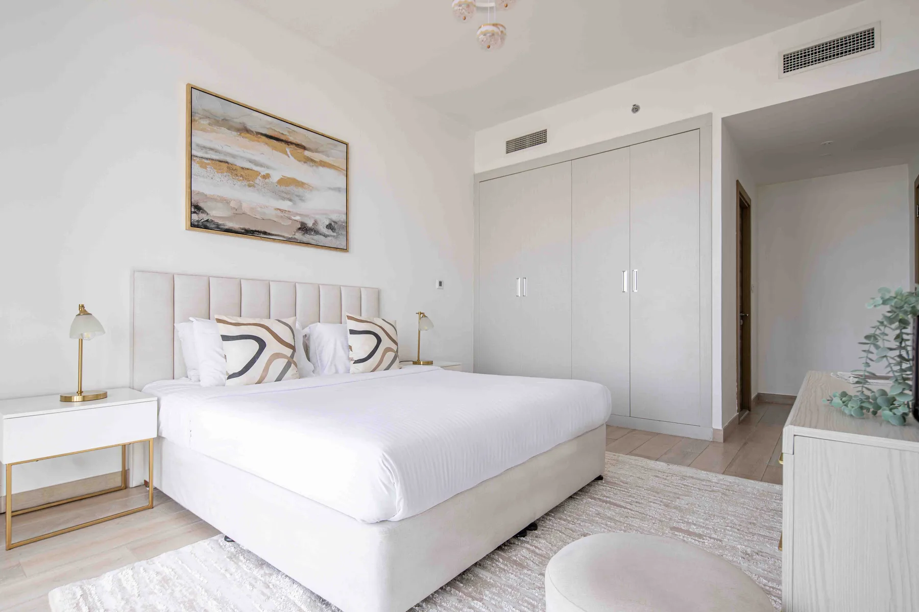 A bright bedroom with a large bed, bedside tables, and a built-in wardrobe.
