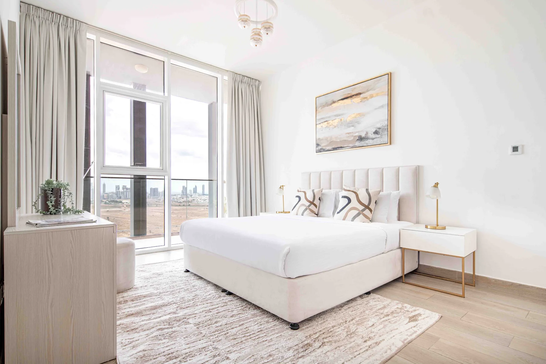 A bright bedroom with a large bed, bedside table, and tall windows.