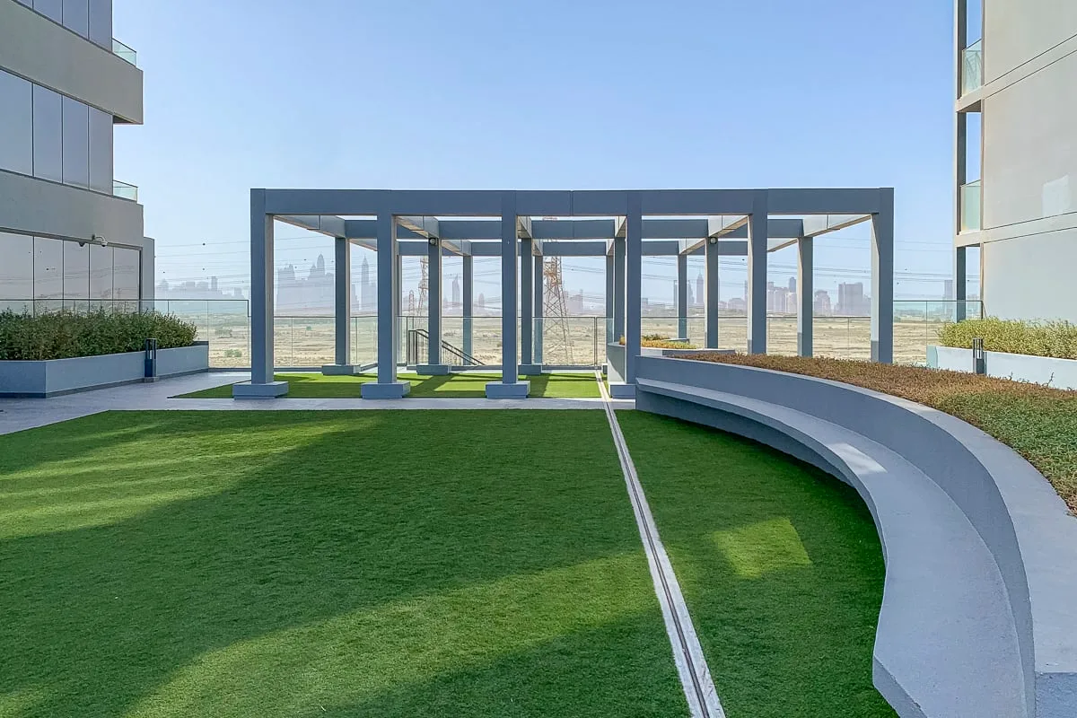 A landscaped outdoor courtyard with a curved concrete bench and open metal pergola.