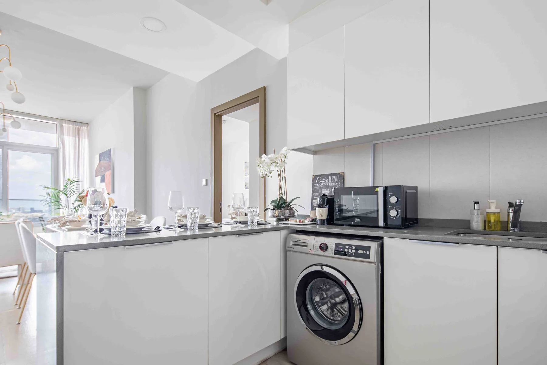 A bright kitchen with a washing machine beneath the counter and a dining table by the window.