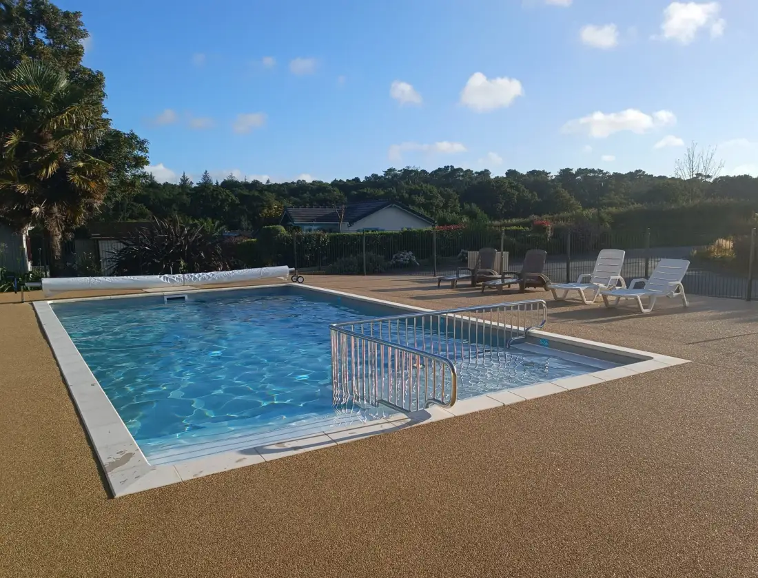 An outdoor swimming pool sits beside several lounge chairs under a clear sky.