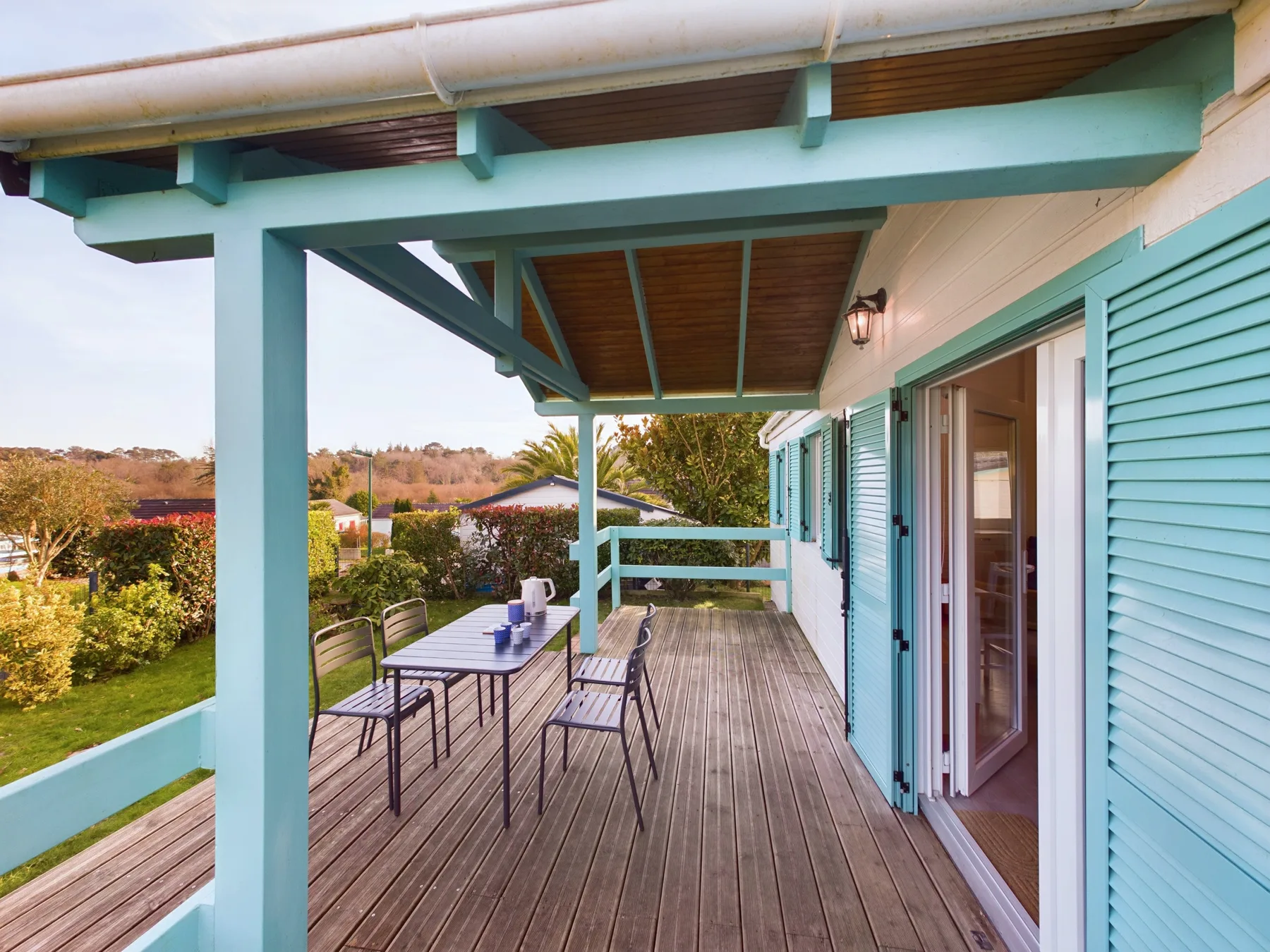 A covered wooden deck has outdoor seating beside turquoise shutters.