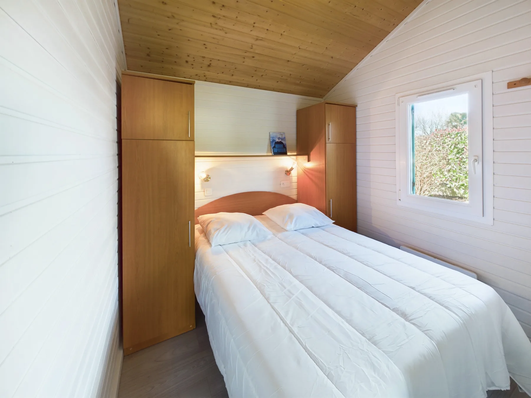 A bedroom with a double bed between two tall wooden wardrobes.
