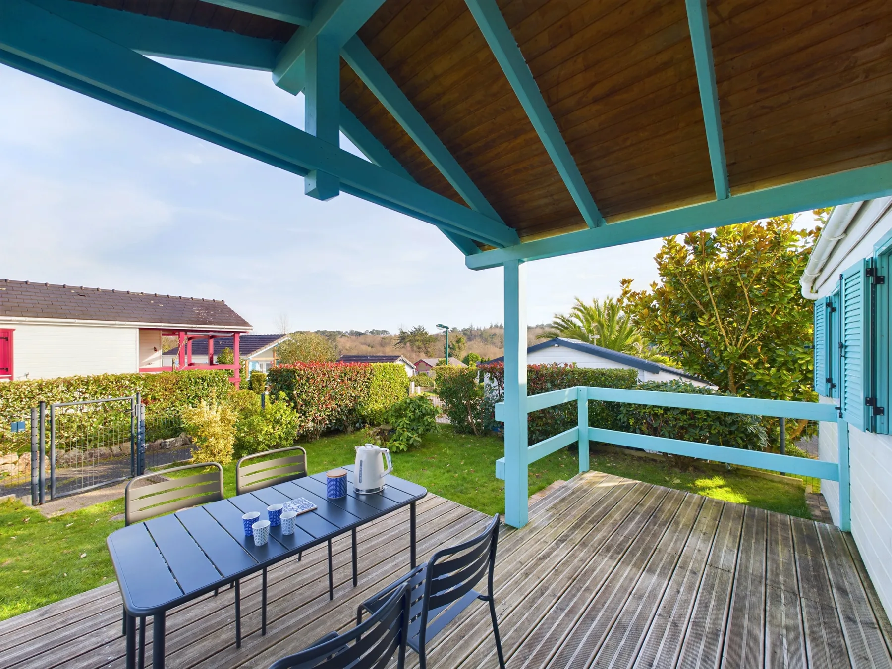 A covered wooden deck with outdoor seating overlooks a garden.