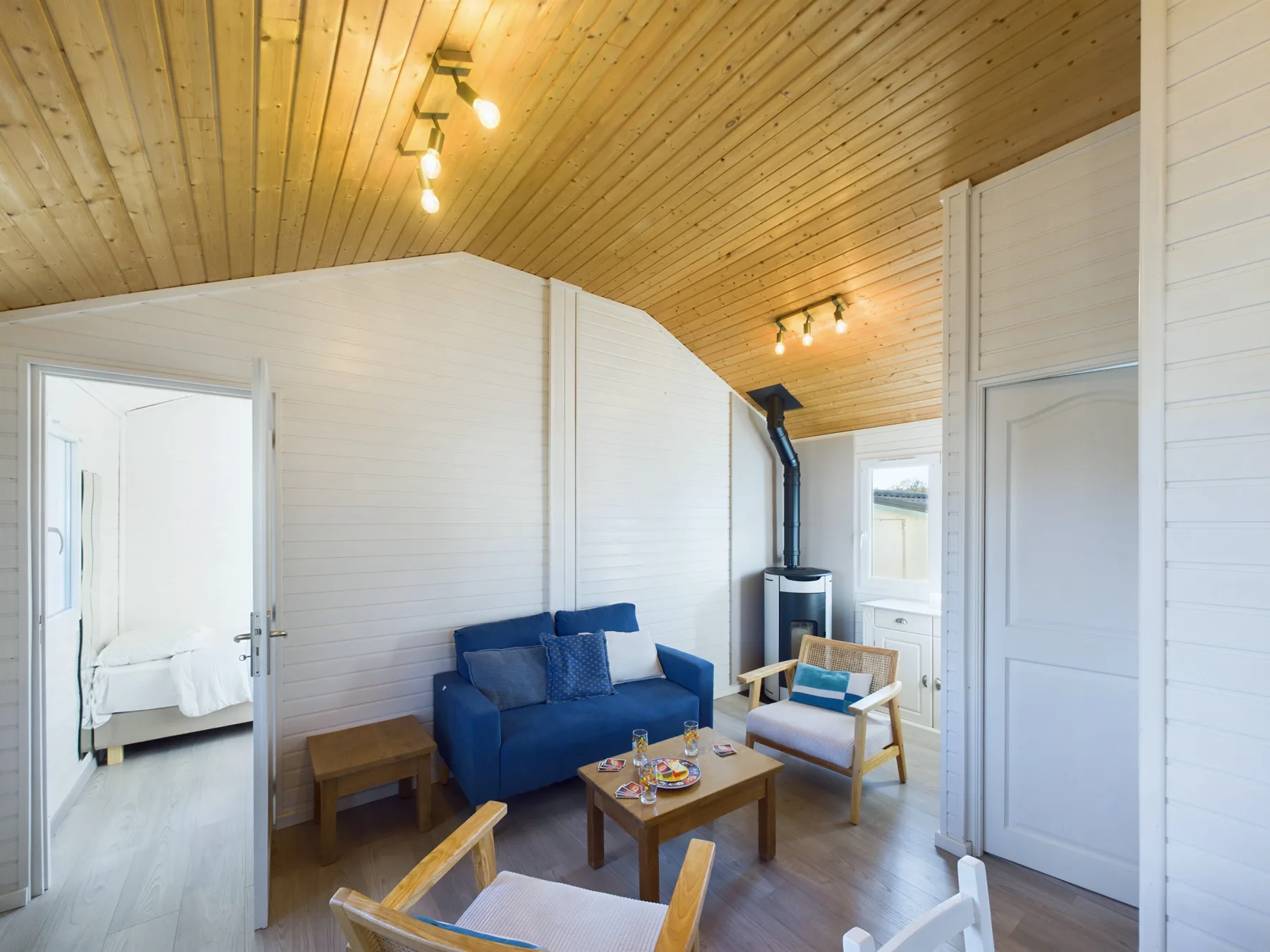 A bright living room with blue seating beneath a wood-paneled ceiling.