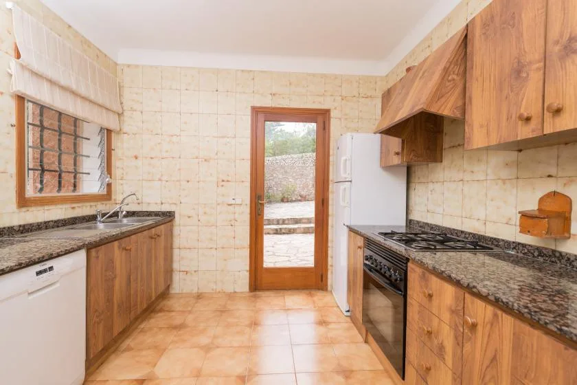 A tiled kitchen with wooden cabinets, a refrigerator, and a glass door opening outside.