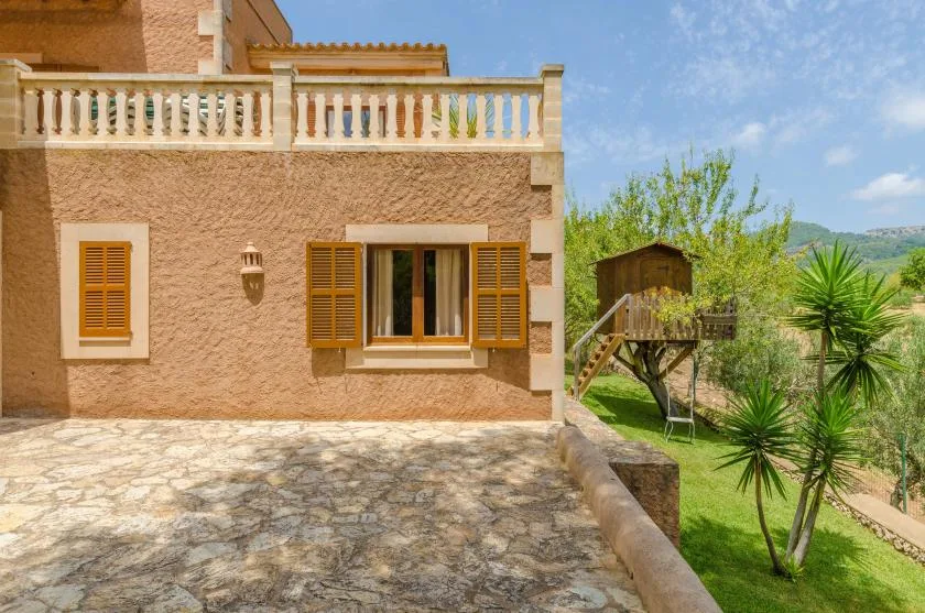 A house exterior overlooks a stone-paved patio and a leafy garden.