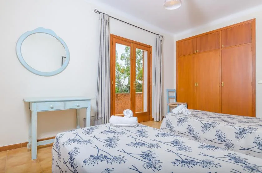 A bedroom with a floral bedspread, a small dressing table, and a wooden wardrobe.