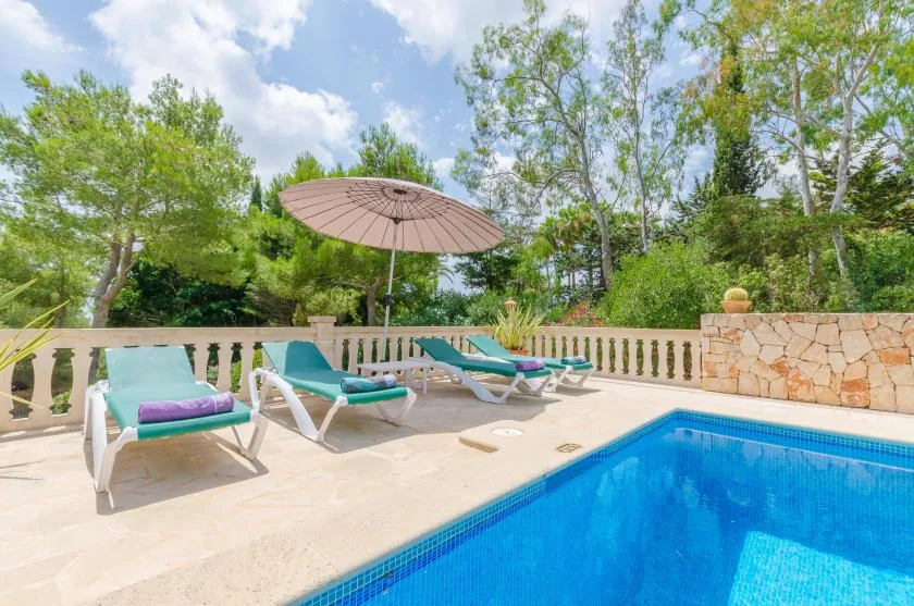 An outdoor pool beside a sunlit patio with loungers and an umbrella.