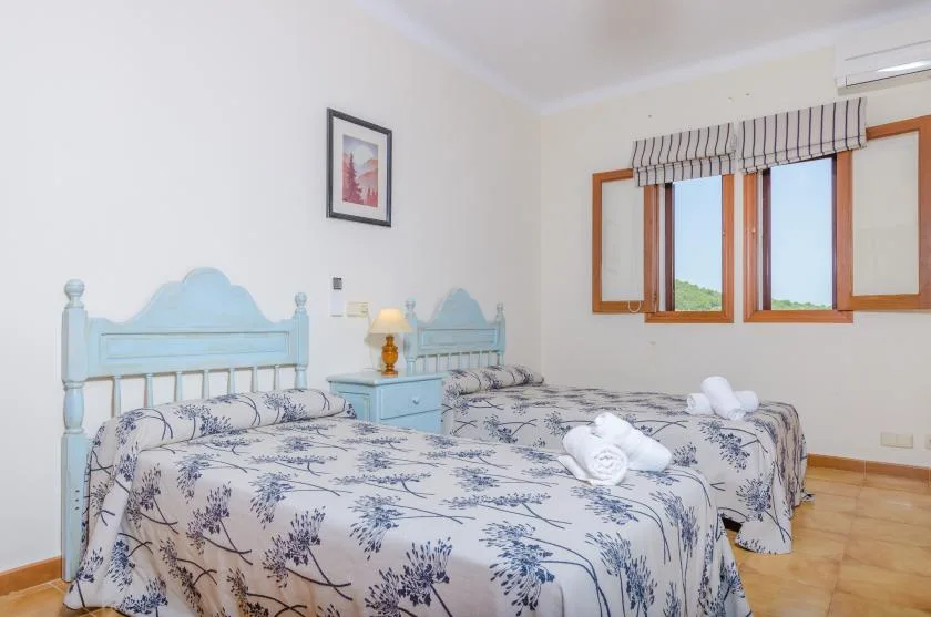A bedroom with two beds and a window overlooking greenery.