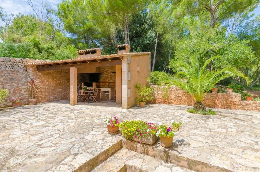 A stone-paved patio surrounds a covered outdoor dining area, with greenery nearby.