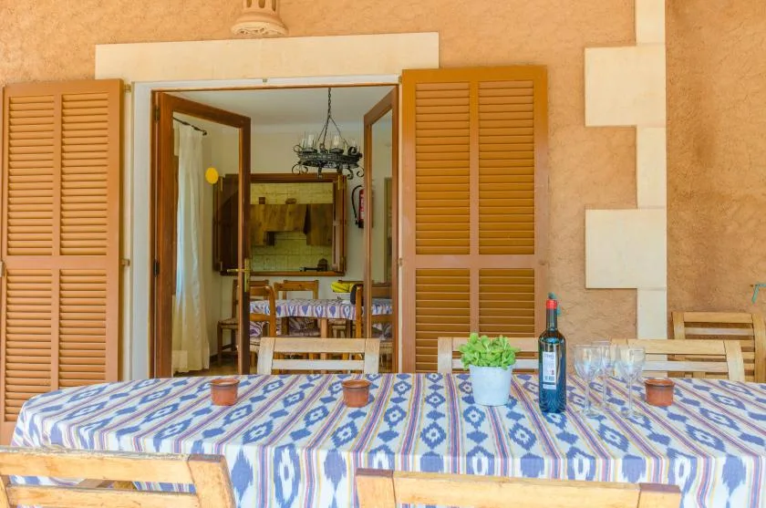A covered dining area with a patterned tablecloth and open wooden shutters.