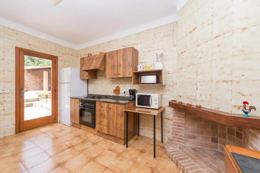 A tiled kitchen with wooden cabinets, a refrigerator, and a built-in brick barbecue.