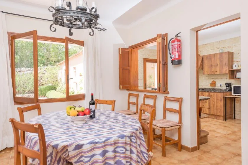 A dining area with a table set near open windows and a doorway to the kitchen.