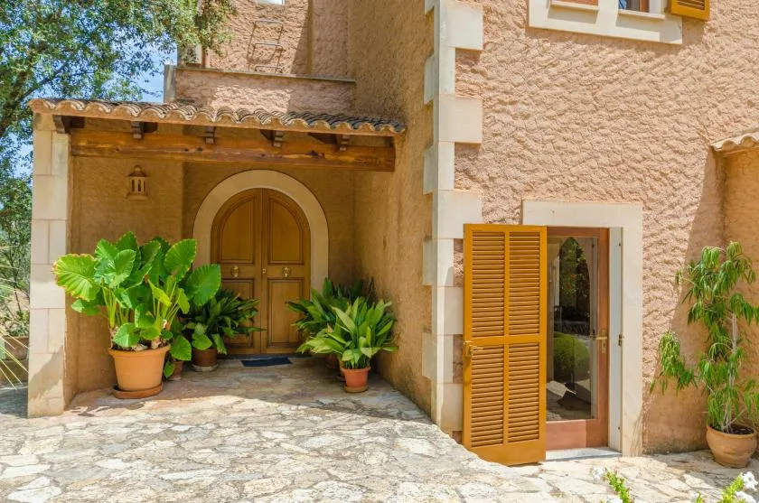 A stone-paved entrance leads to an arched wooden door, with potted plants nearby.