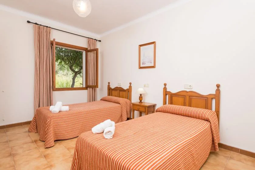 A bedroom with two beds, striped bedspreads, and a window overlooking a tree.