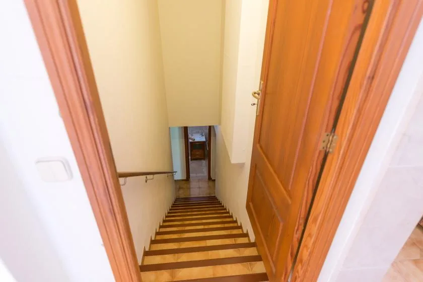 A narrow indoor staircase descends between cream-colored walls toward a doorway.