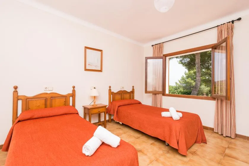 A twin bedroom with two single beds and a window overlooking trees.