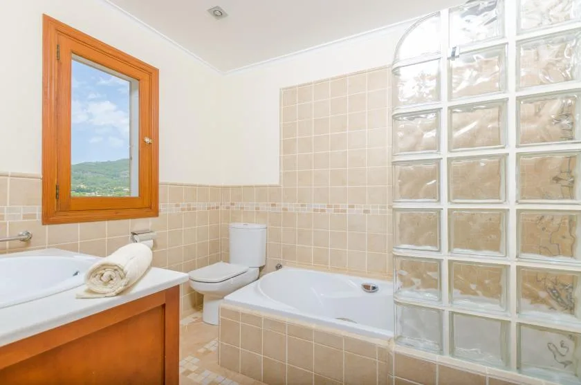 A bright bathroom with a bathtub, sink, and glass-block wall.