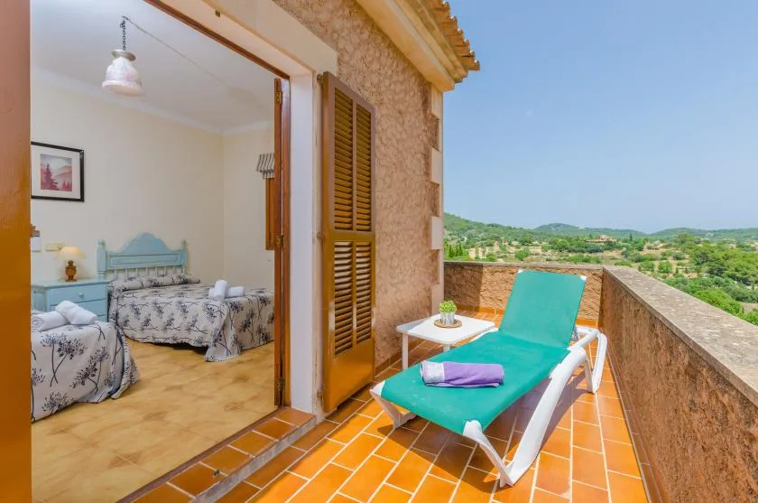 A tiled balcony with lounge seating overlooks a green landscape.