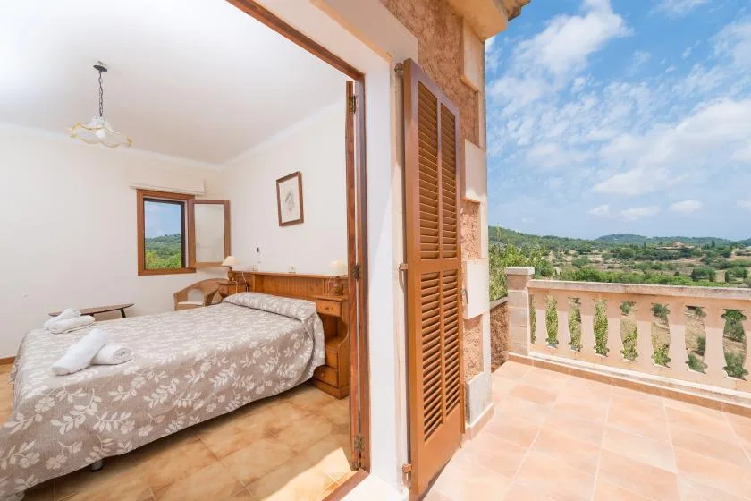 A bedroom opens onto a tiled balcony overlooking a green landscape.