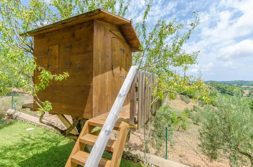 A small wooden structure stands among greenery on a sunny hillside.