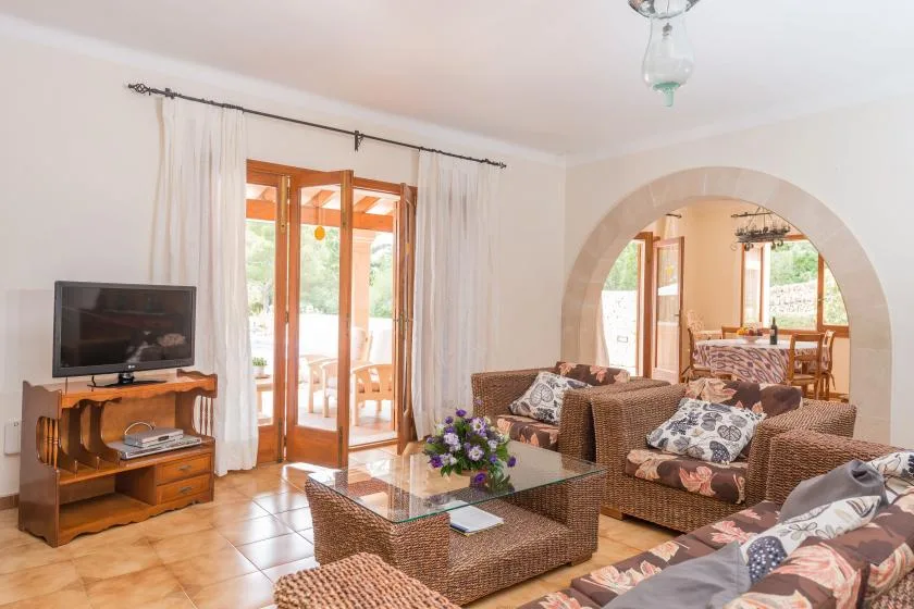 A living room with wicker seating, a glass coffee table, and a television.