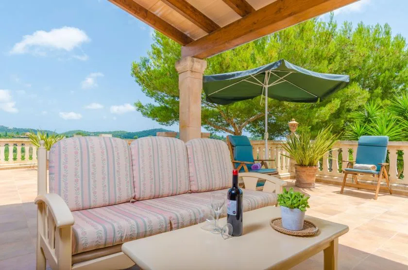 A covered outdoor patio with cushioned seating, a table, and a large umbrella.