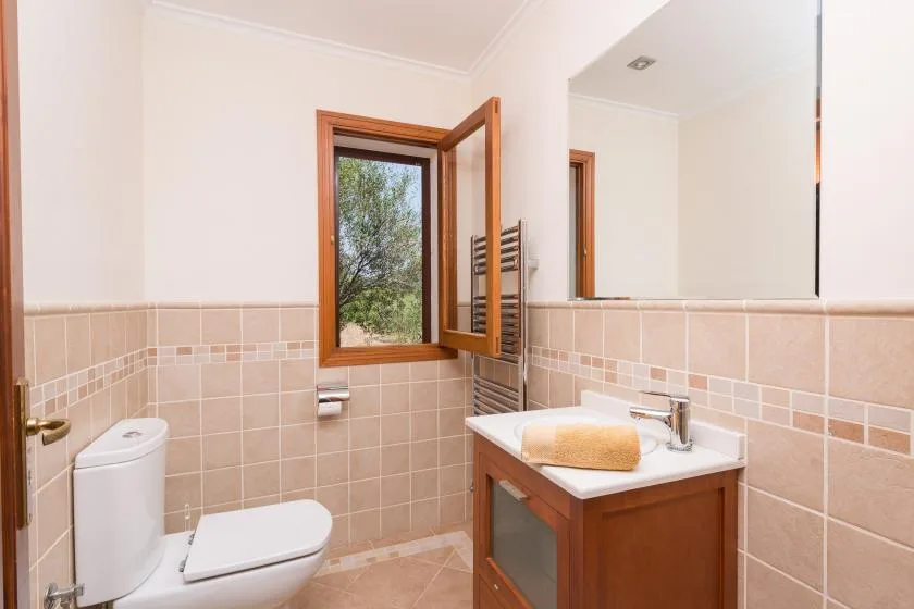 A tiled bathroom with a sink, toilet, and open window.