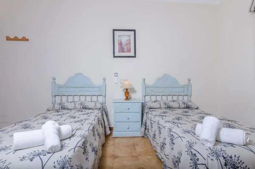 A bedroom with two beds, a nightstand, and a lamp.