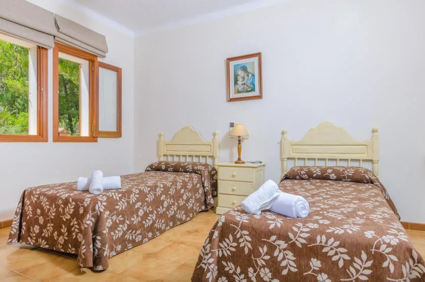 A bedroom with two beds, patterned bedspreads, and a window overlooking greenery.
