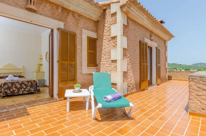 A sunlit tiled terrace with a lounge chair and a view of the surrounding landscape.