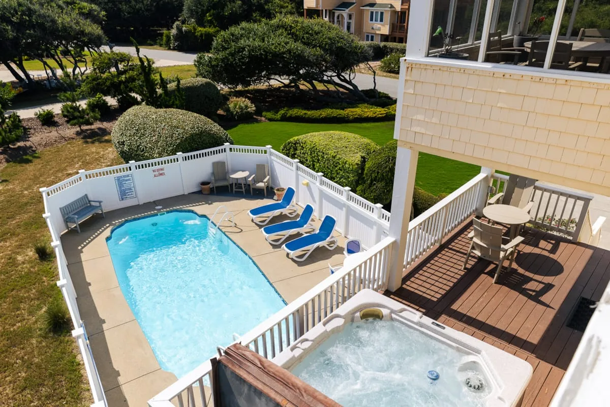 Una piscina y un jacuzzi al aire libre están junto a una terraza con asientos.