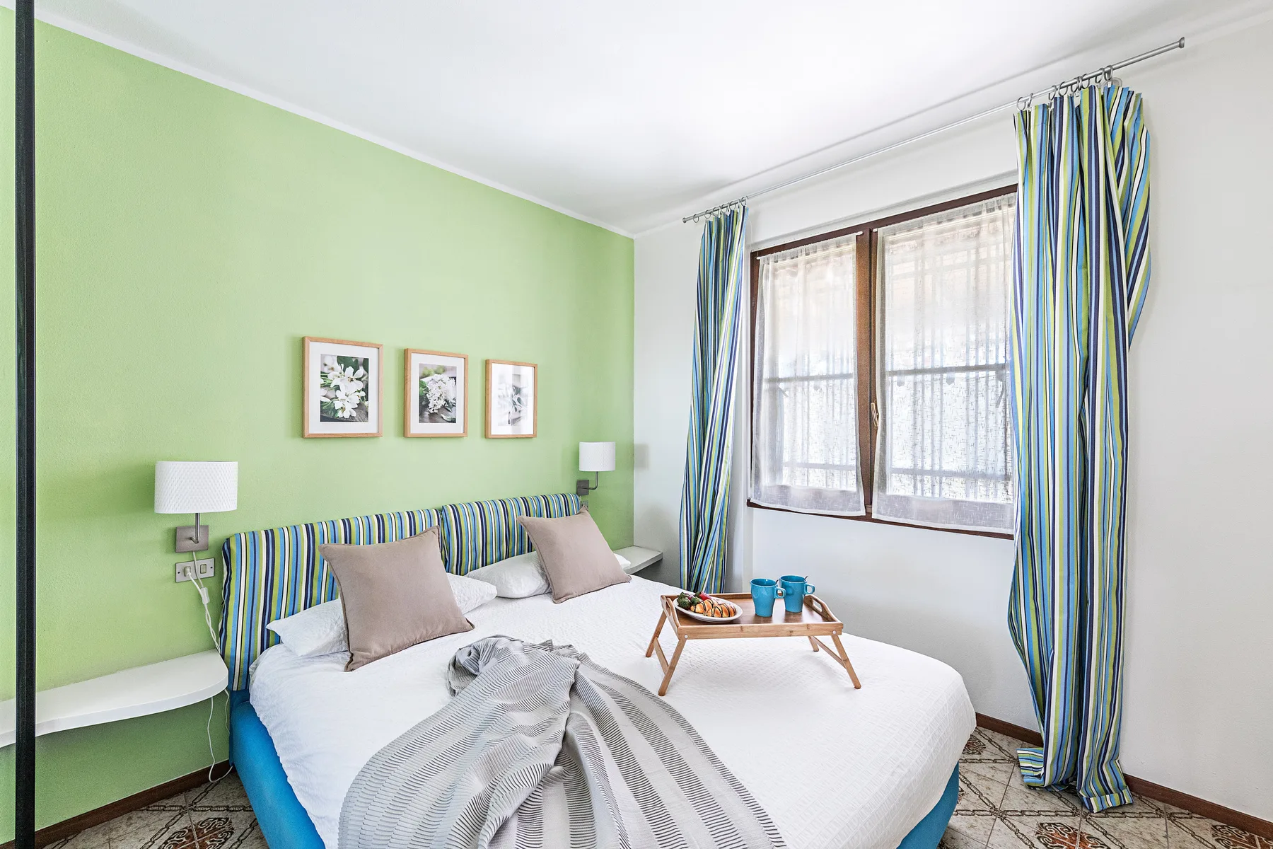 A bright bedroom with a bed, green walls, and striped curtains by the window.