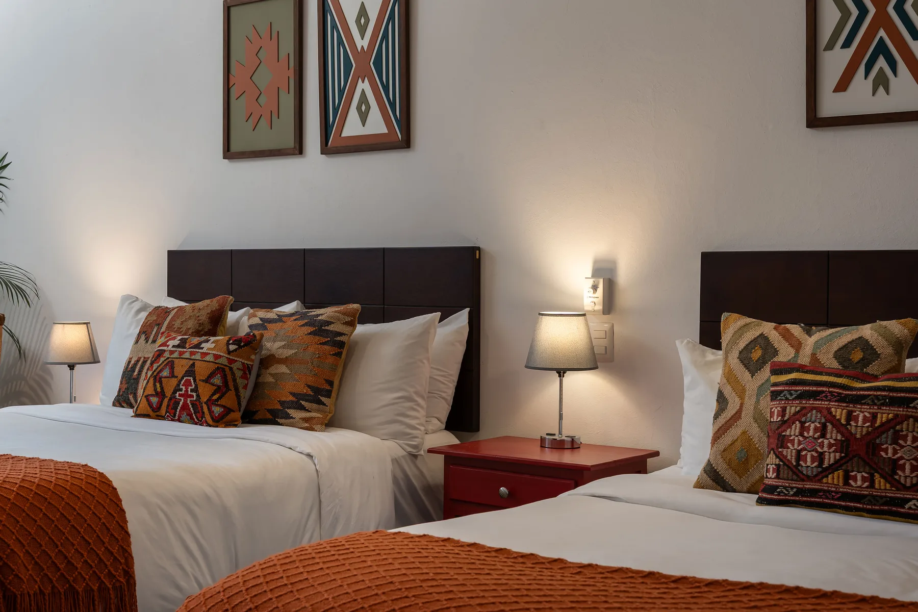 A bedroom with two beds, patterned pillows, and warm bedside lamps.