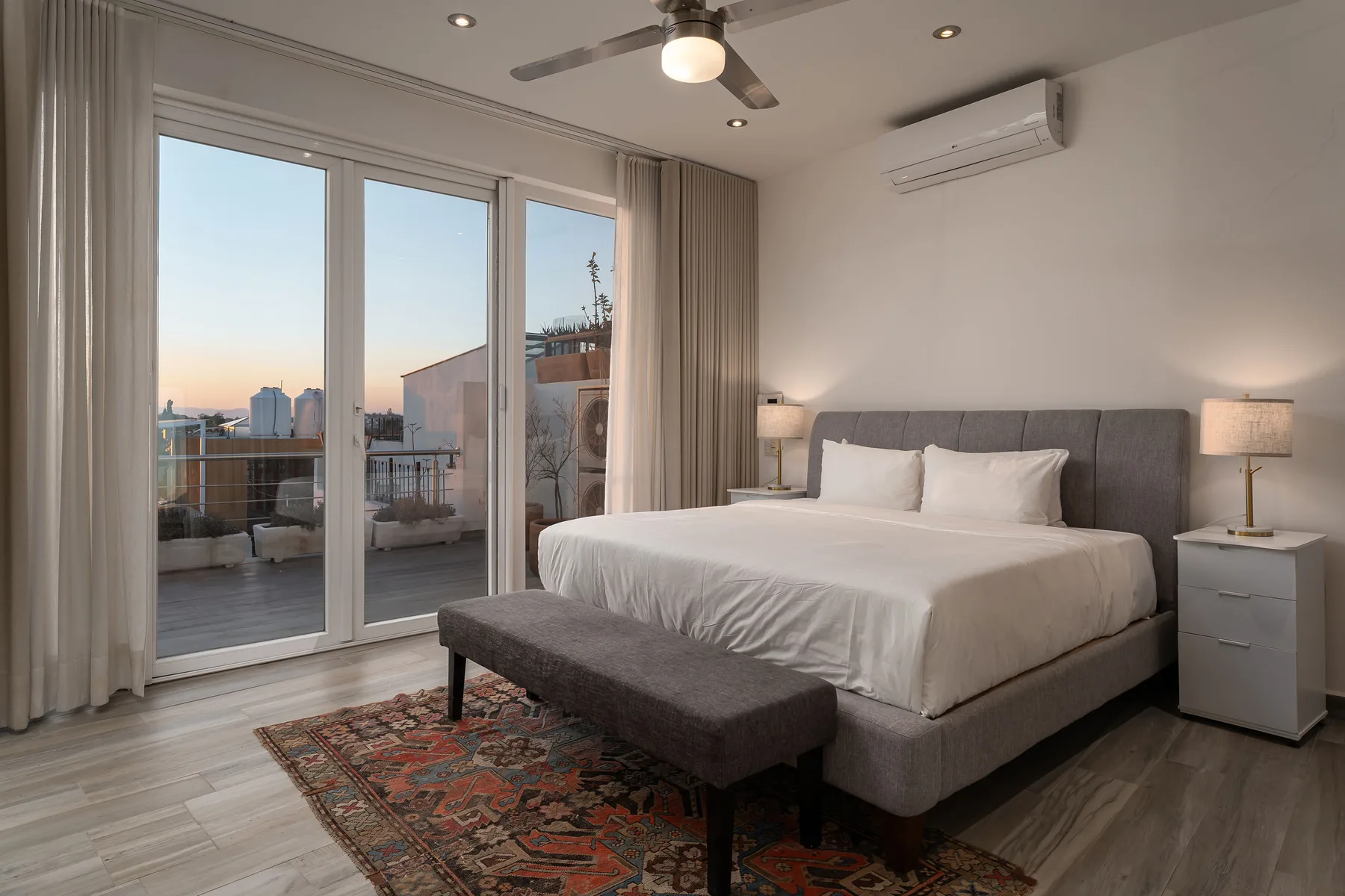 A bedroom with a large bed and floor-to-ceiling windows opening onto a balcony.