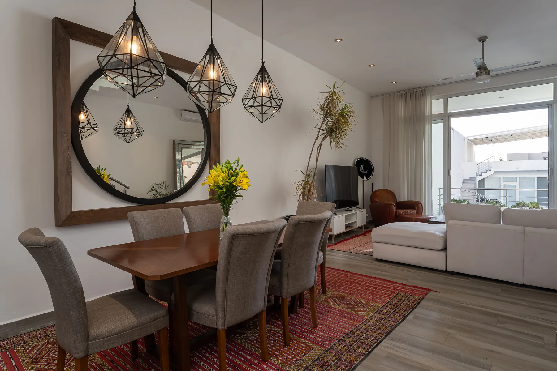 A dining and living area with a wooden table, seating, and large windows.