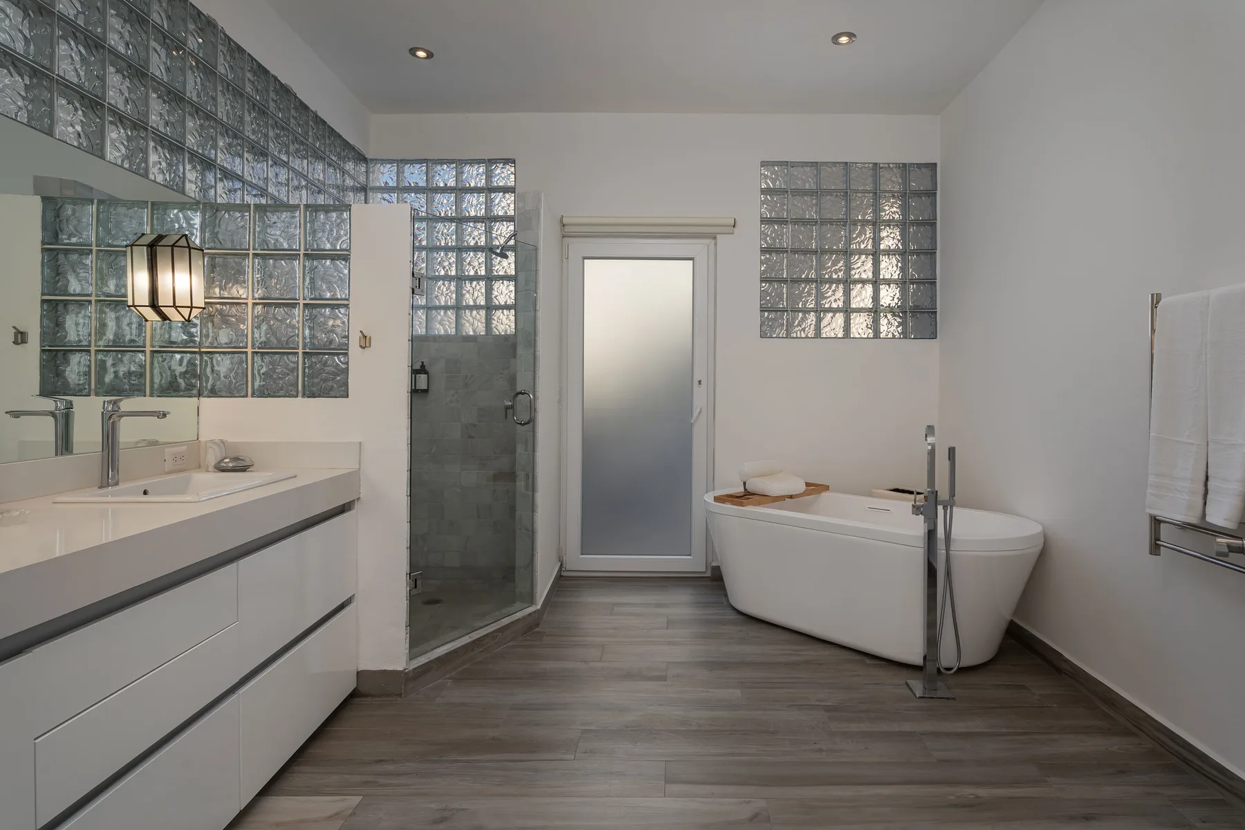 A modern bathroom with a glass shower, bathtub, and long vanity.