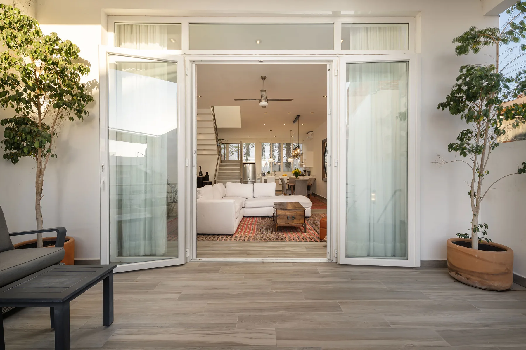 Open glass doors lead into a living room with white seating and a rug.