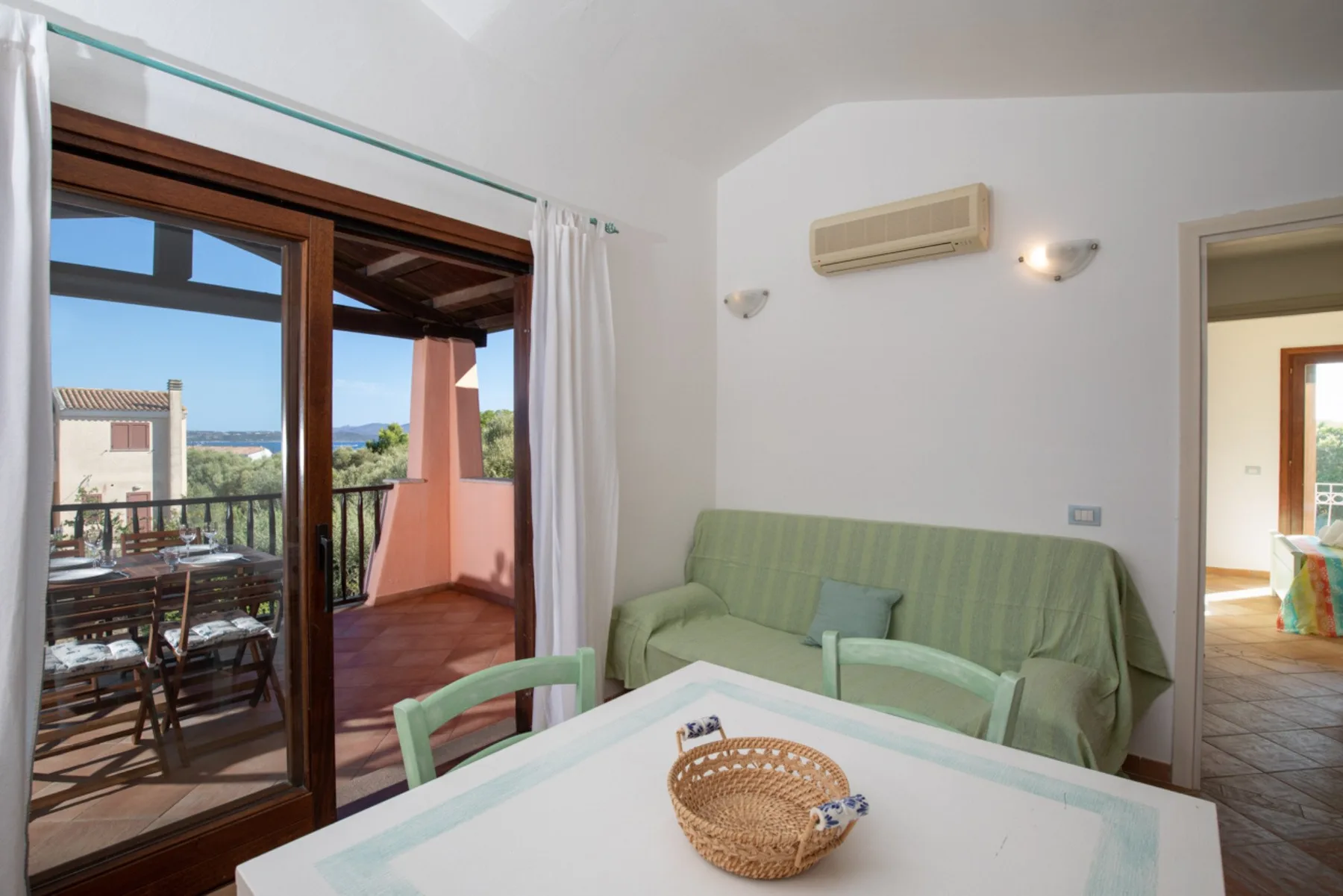 A bright living room with a green sofa and a table beside an open balcony.