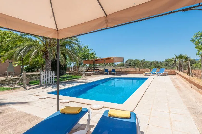 An outdoor swimming pool sits beside a tiled patio with lounge seating.