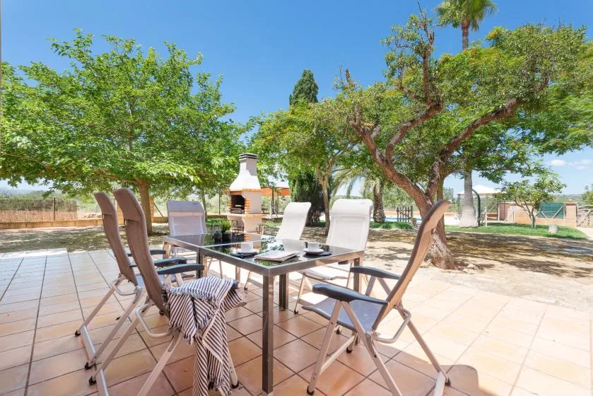 An outdoor dining area with a table and seating beneath leafy trees.