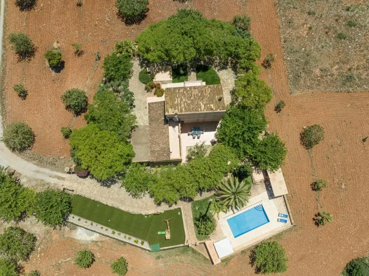 Aerial view of a house surrounded by trees, with a swimming pool and garden.