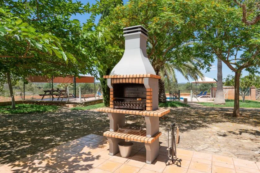 An outdoor barbecue grill stands beneath leafy trees in a paved patio area.
